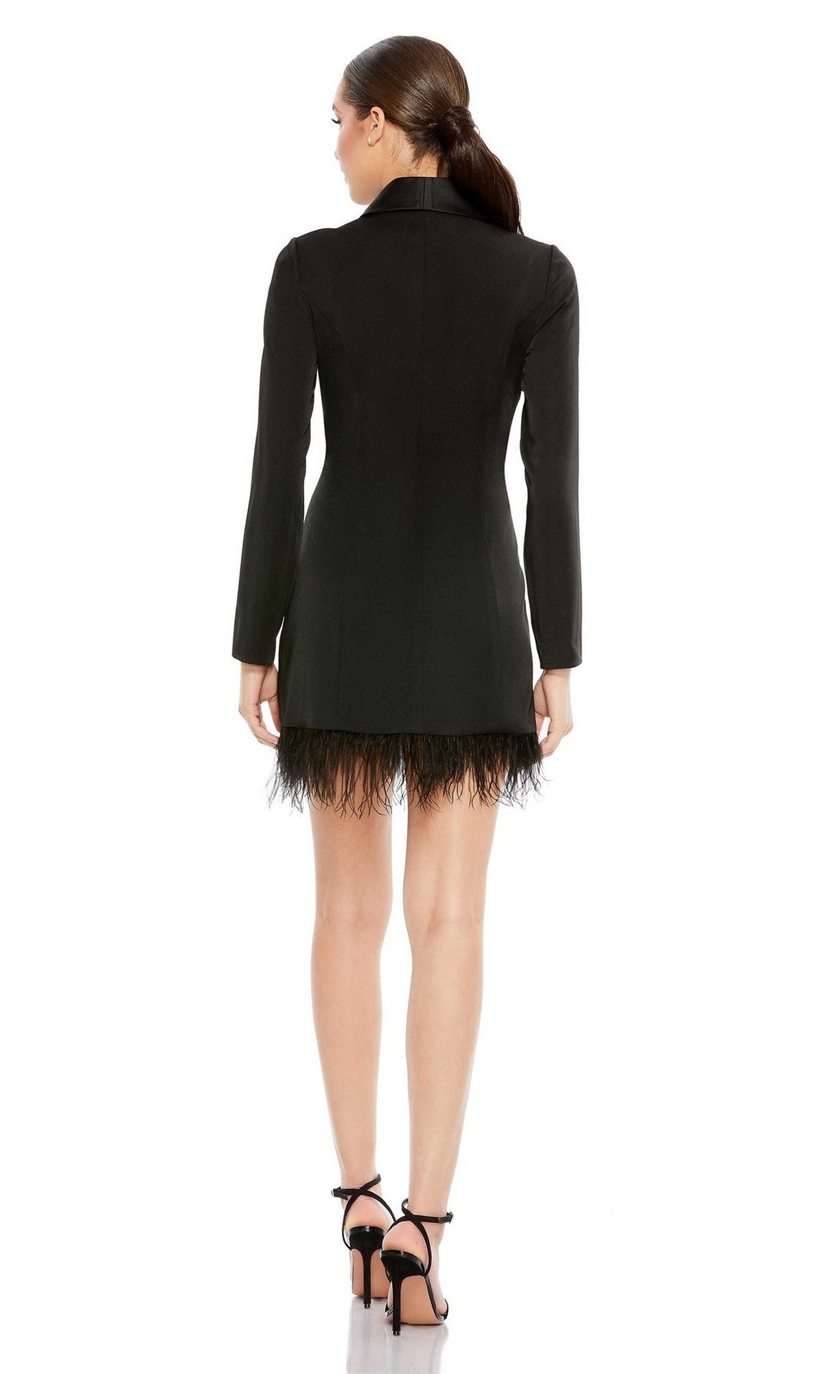 A woman stands with her back to the camera, wearing the Short Party Dress 26510 by Mac Duggal—a black feather tuxedo dress with long sleeves—paired with black high-heeled sandals.